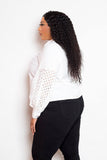 Plus-size model wearing white blouse with punched sleeves and black pants, side view.